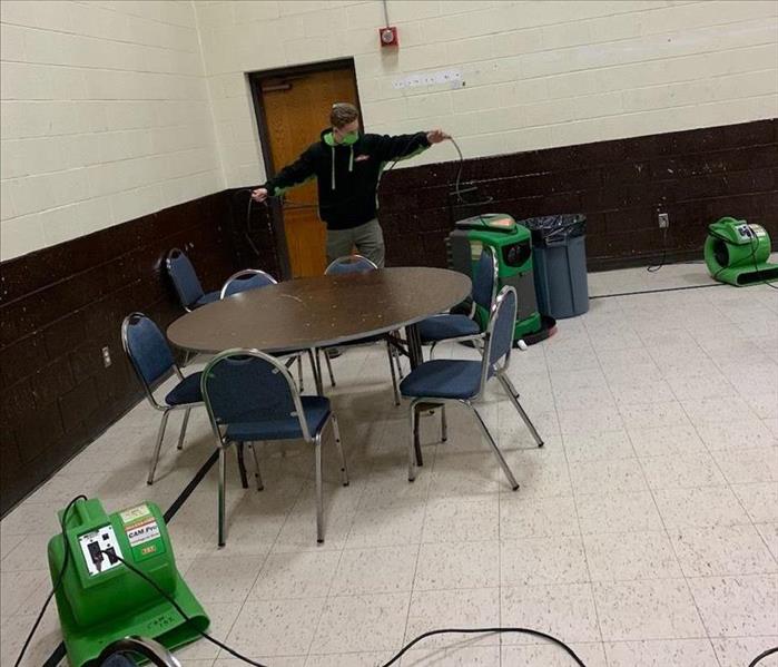 Technician operating SERVPRO air movers and dehumidifiers in a large open dining area