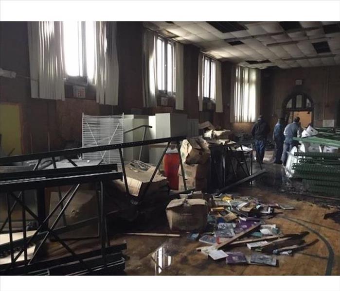 SERVPRO techs in a schoolroom with charred items and smoke damaged ceiling 