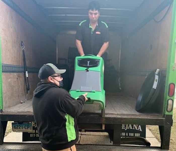 Two technicians unload a low-grain refrigerant dehumidifier from a SERVPRO truck