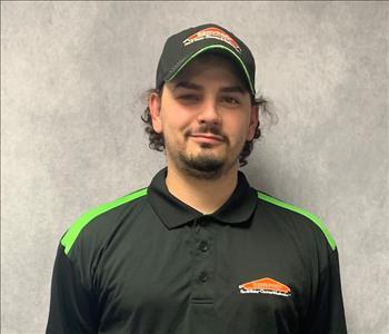 Male employee posing in a black cap and SERVPRO logo hoodie